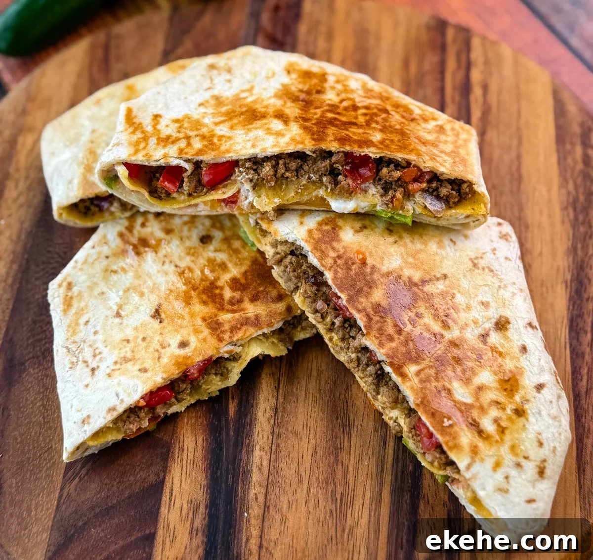 Golden brown beef and cheese crunchwrap supreme cut in half and stacked on a wooden cutting board with halved limes in the background