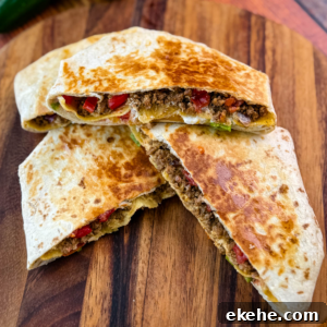 Golden brown beef and cheese crunchwrap supreme cut in half and stacked on a wooden cutting board with halved limes in the background.