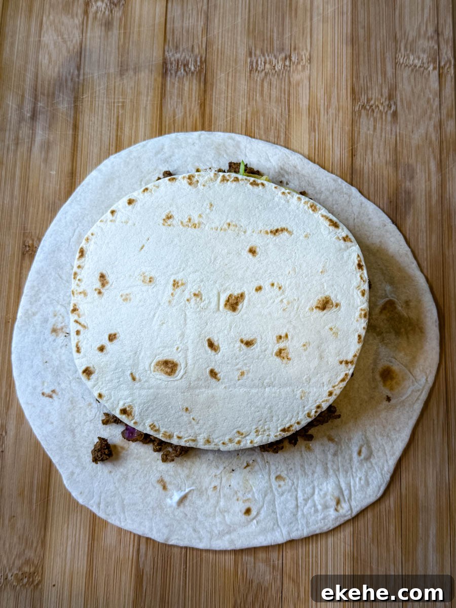 Small flour tortilla placed over the beef and cheese filling on a larger tortilla, ready to be folded into a crunchwrap.