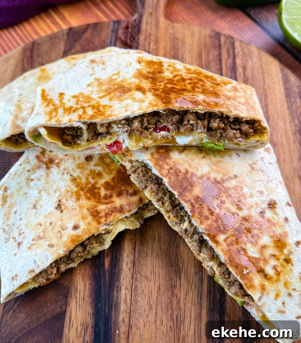 Golden brown beef and cheese crunchwrap supreme cut in half and stacked on a wooden cutting board with halved limes in the background