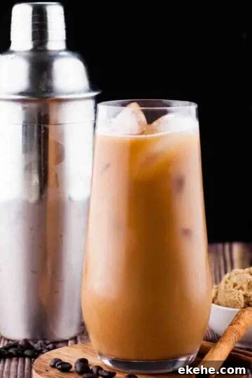 Brown sugar shaken espresso in a tall glass with a cocktail shaker and brown sugar in the background.