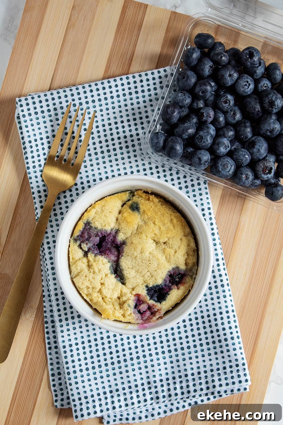 overhead view of keto blueberry mug cake in a ramekin next to a gold fork