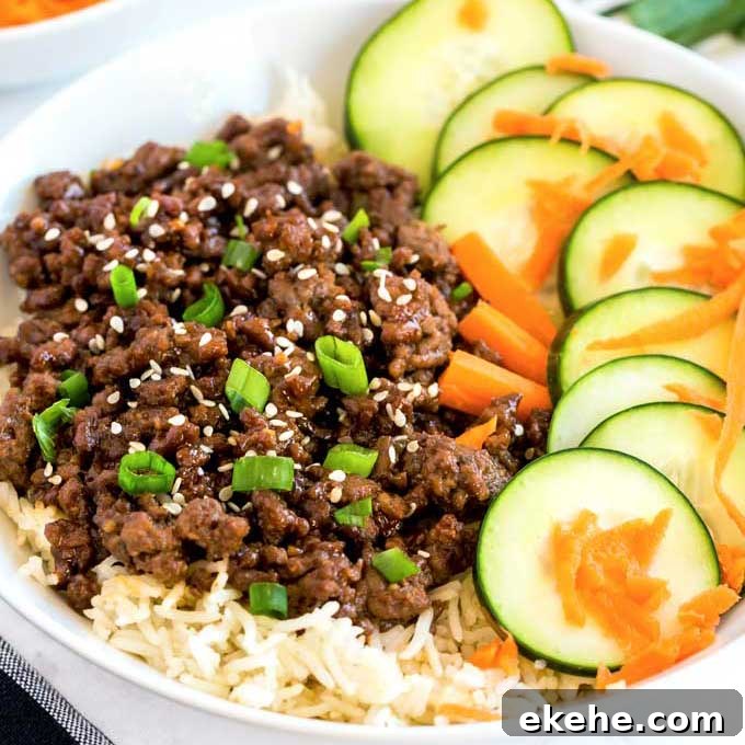 Korean ground beed over rice with cucumbers and carrots served in a white bowl.