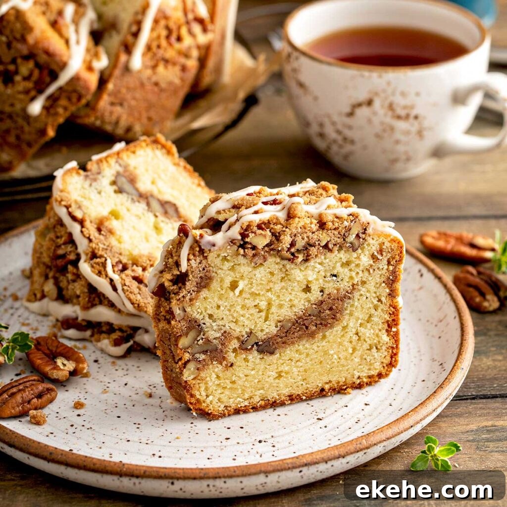 A slice of Sour Cream Coffee Cake loaded with a ribbon of cinnamon-sugar strudel running through the middle, pecans, cinnamon-sugar crumb topping and drizzled with maple glaze