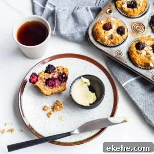 A plate with an apple blackberry muffin split open, served with butter and a cup of tea.