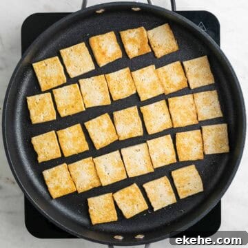 Pan-fried tofu slices in a skillet.