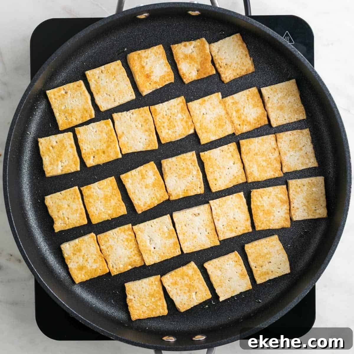 Pan-fried tofu slices in a skillet.