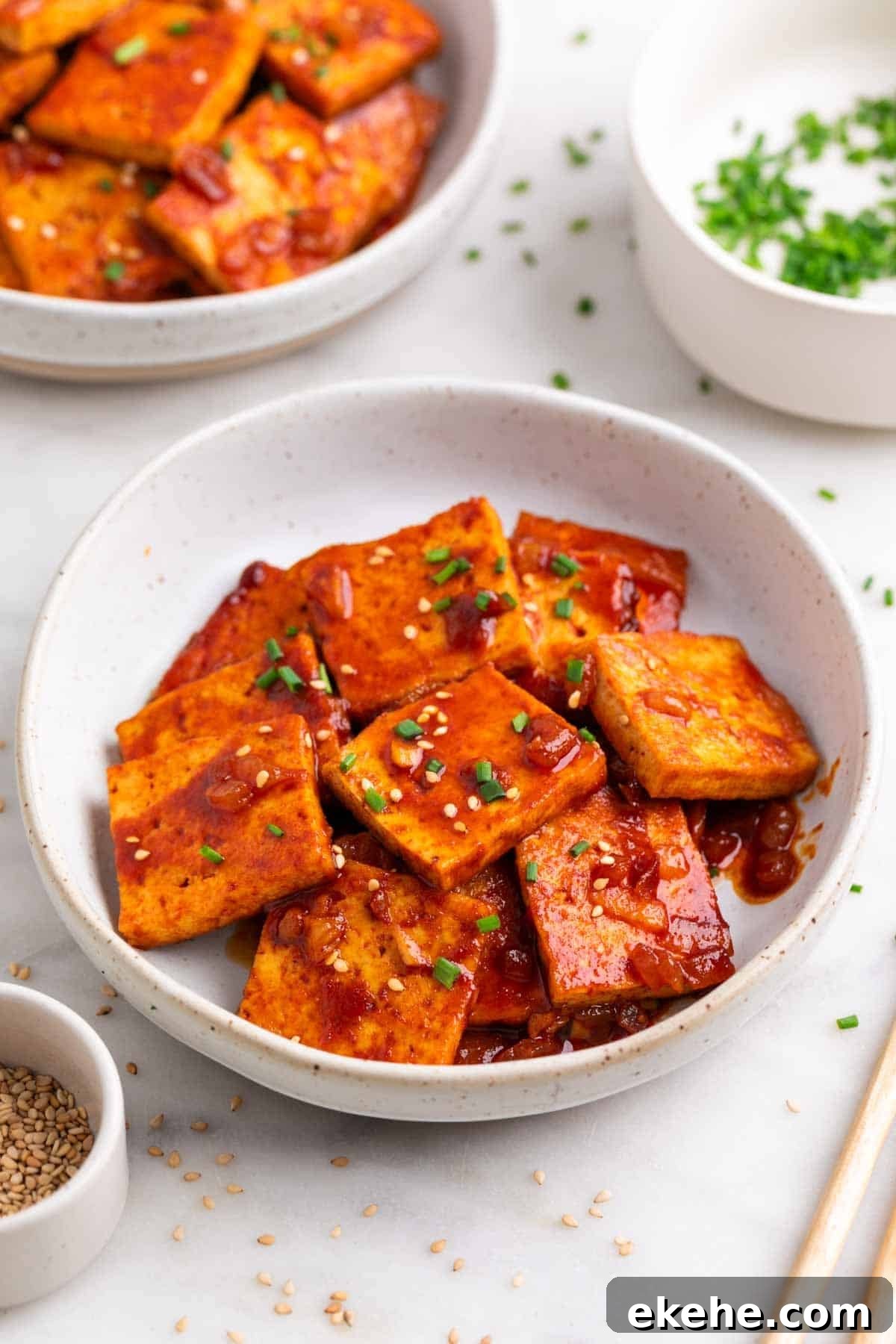 Spicy tofu garnished with sesame seeds and chives, served with chopsticks.