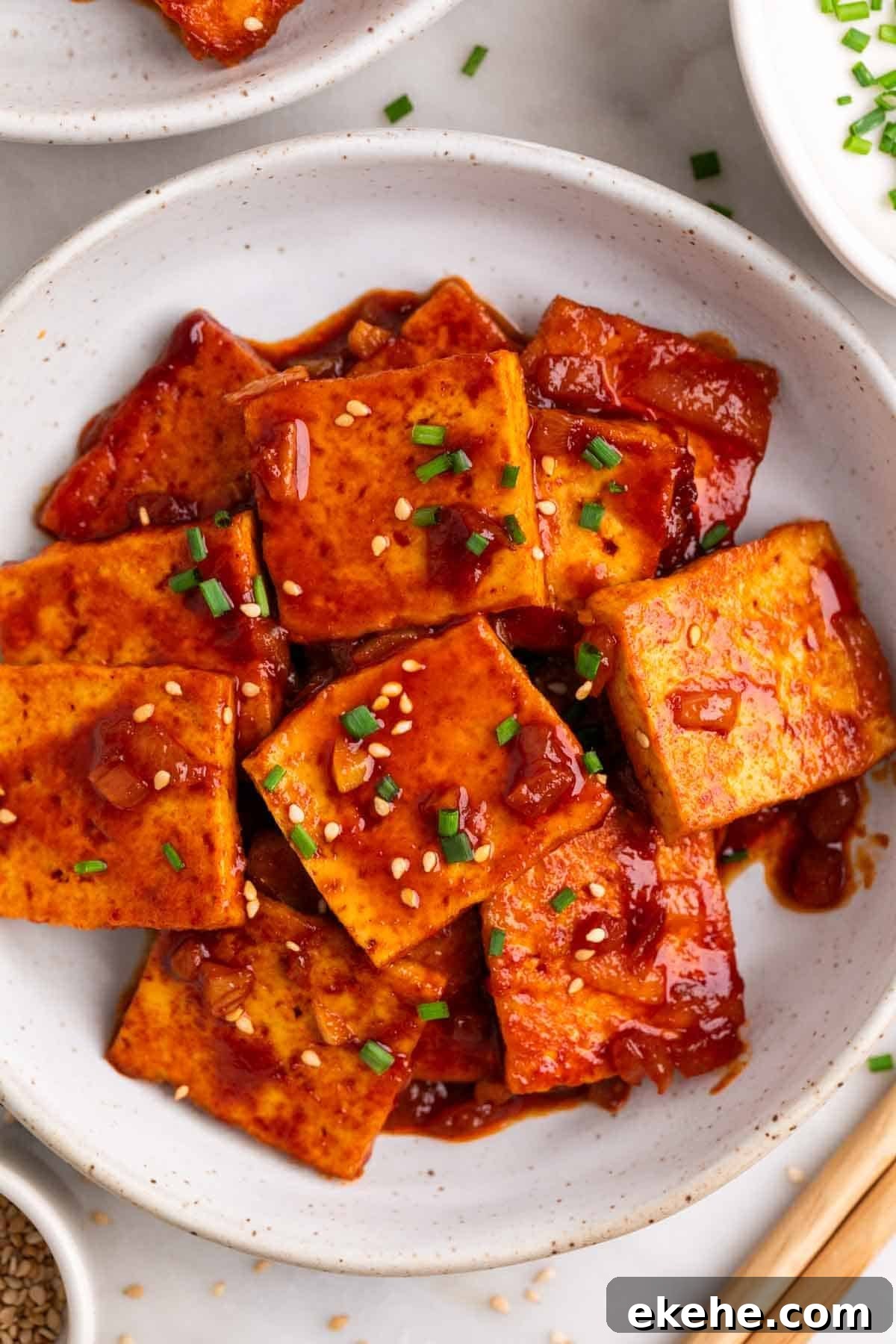 Spicy tofu topped with sesame seeds and chives, chopsticks on the side.