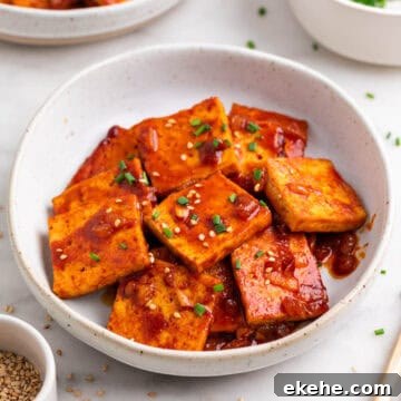 Korean-inspired spicy tofu with chopsticks, sesame, and chives.