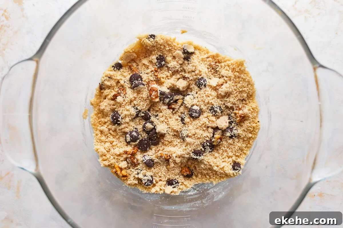 chocolate chips and walnuts added to crumbly cookie dough in a glass bowl.