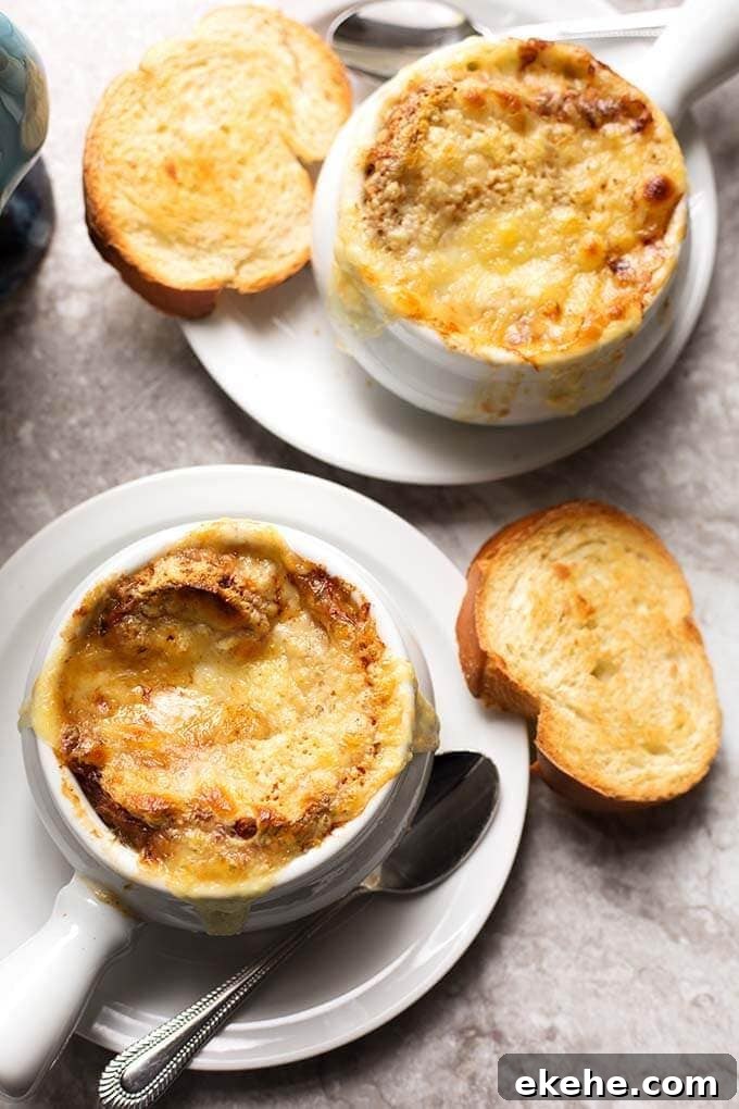 Top view of two bowls of French Onion Soup with melted cheese and small slice of toasted bread on white plates