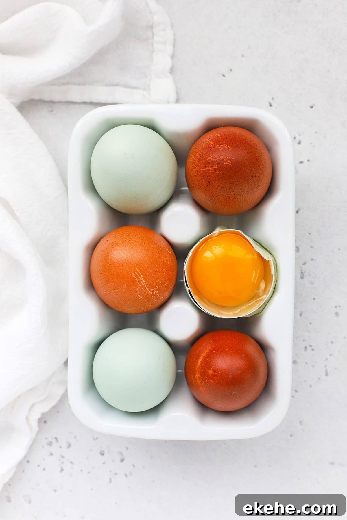Overhead view of an egg carton with 6 eggs. One egg is open, revealing a golden yolk