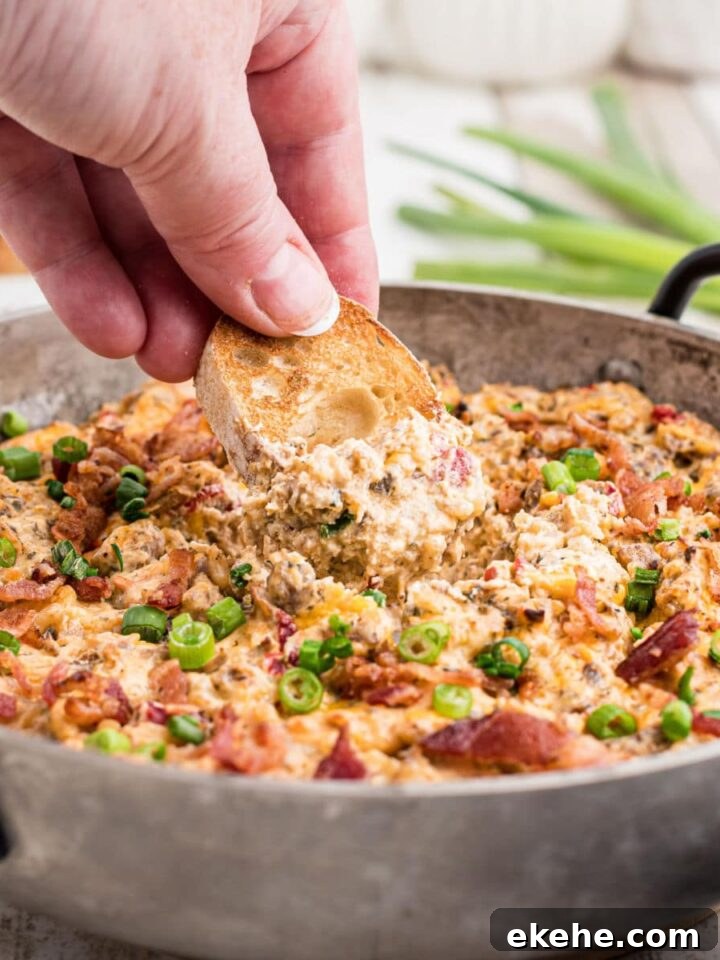 a skillet with some boudin dip cooked and some green onions sprinkled on top with a hand dipping into the dip