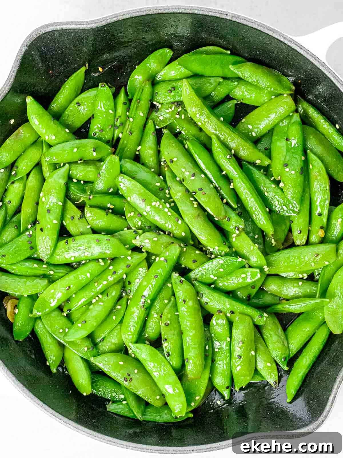 Asian style sugar snap peas with garlic and black and white sesame seeds in a dark pan.