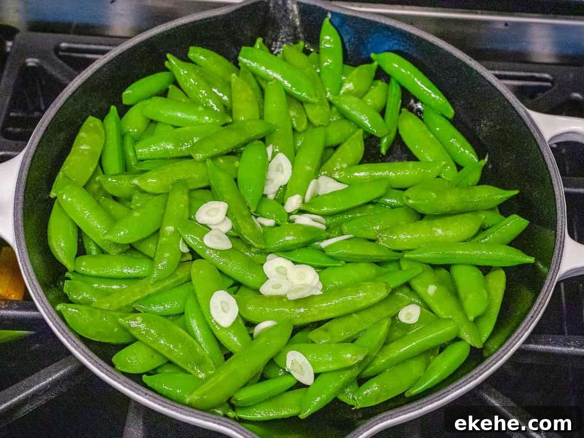 Sugar snap peas with garlic being sauteed in a dark pan.
