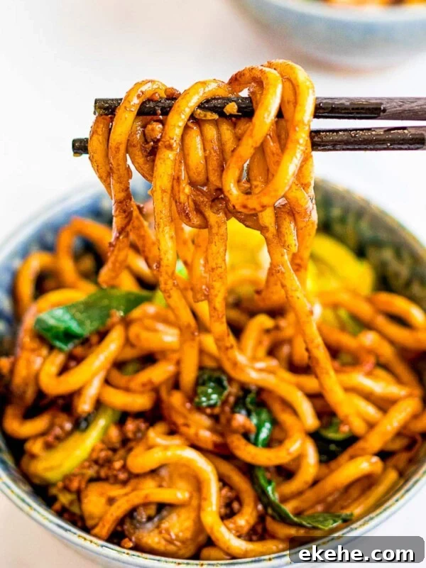 a bowl of yaki udon, stir fried udon noodles held by chopsticks