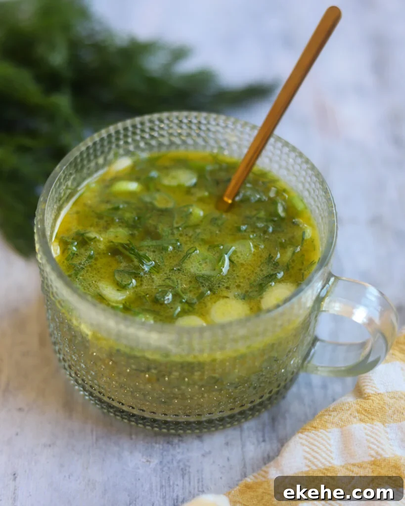Close up view of a bowl of healthy dill Dijon salad dressing made with green onions, maple syrup, vinegar, mustard and dill. The bowl is on a gray surface surrounded with dill leaves and a checkered cloth.