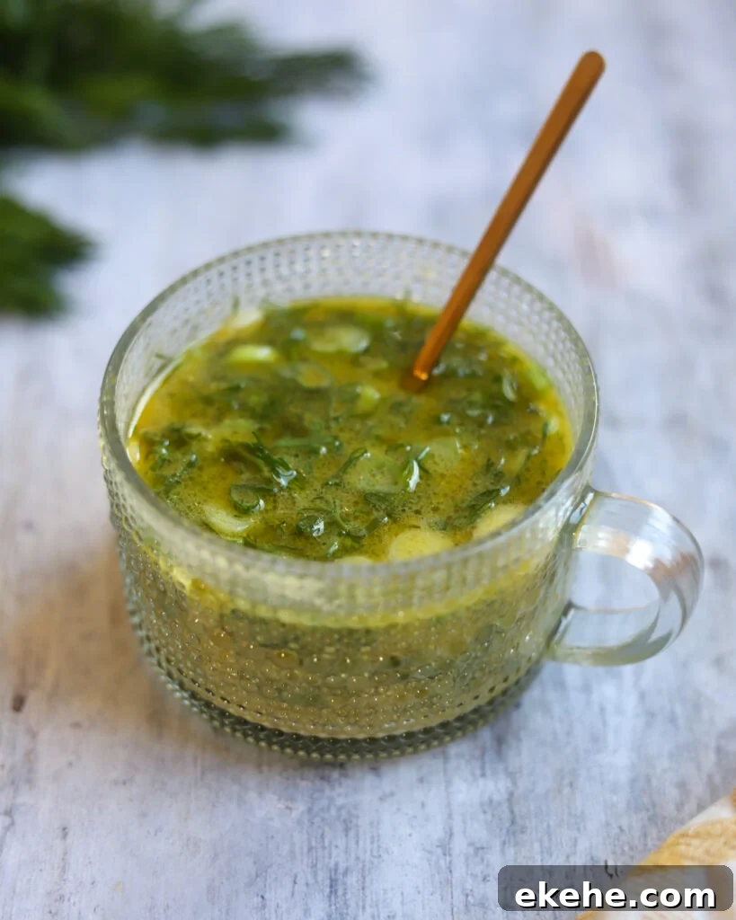 Closeup view of a glass serving dish with vegan dill salad dressing in it sits on a gray surface with fresh dill in the background.