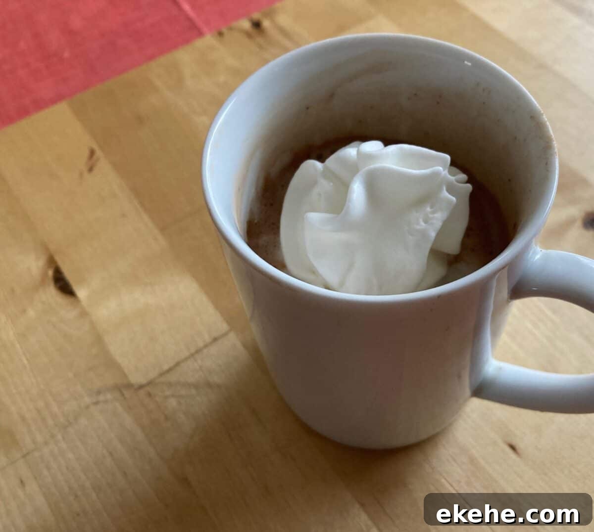 White mug of sugar-free hot chocolate with light whipped topping on butcher block.
