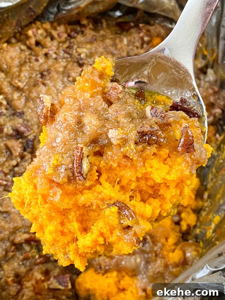 Close up silver serving spoon loaded with candied sweet potato casserole over top of a slow cooker