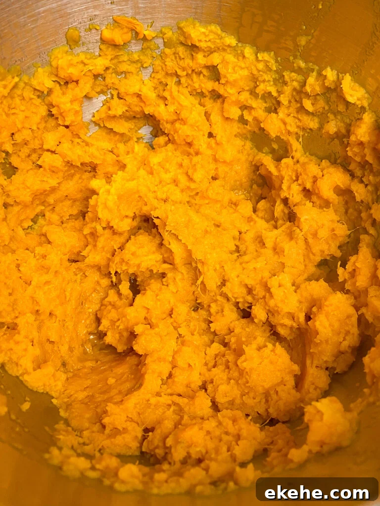 Freshly mashed warm sweet potatoes in a silver mixing bowl