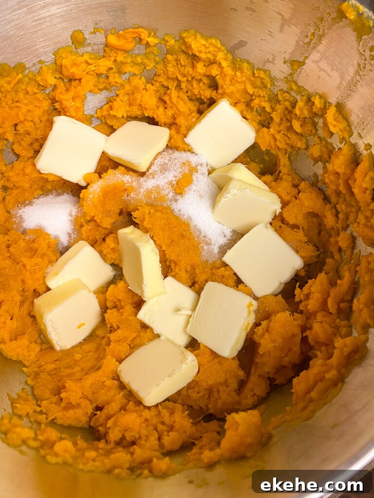 Pats of butter and sugar spread out over freshly mashed sweet potatoes in a mixing bowl