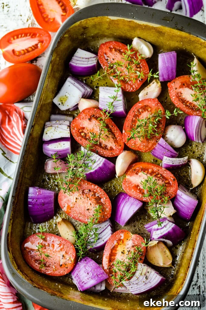 Tomatoes, garlic and red onions and sprigs of thyme are in a stoneware baking pan.