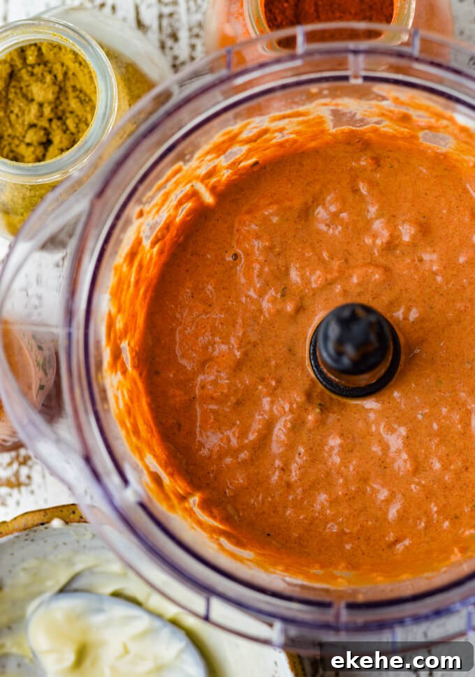 Spicy Roasted Tomato and Garlic Aioli is blended in a food processor. Bowls of mayonnaise, cumin and smoked paprika sit next to the food processor.