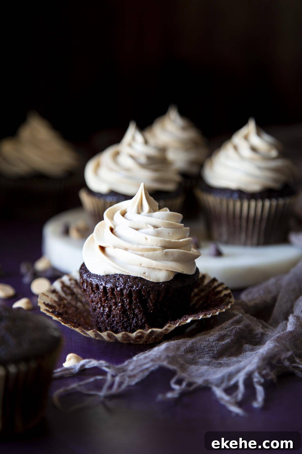 A chocolate peanut butter cupcake with the cupcake paper peeled off, more cupcakes in the background