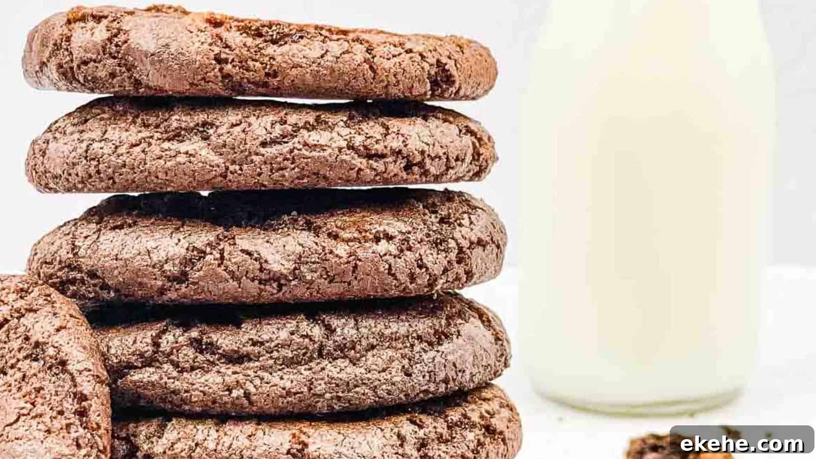 A stack of chocolate cookies with a bottle of milk in the background on a white surface.