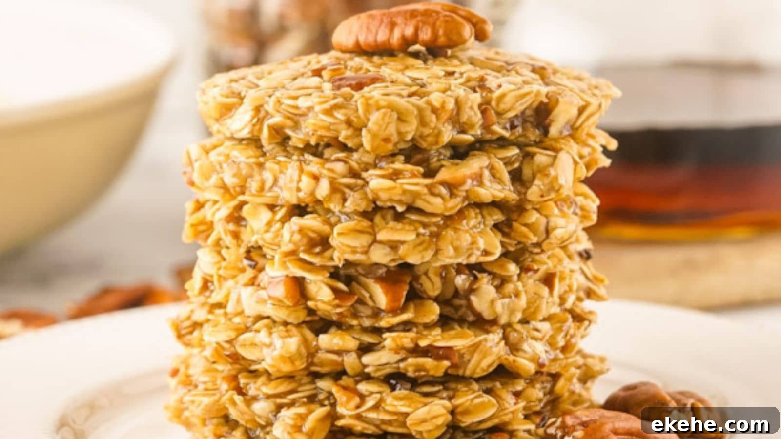 A stack of no-bake maple pecan cookies on a white plate, with syrup and a bowl in the background.