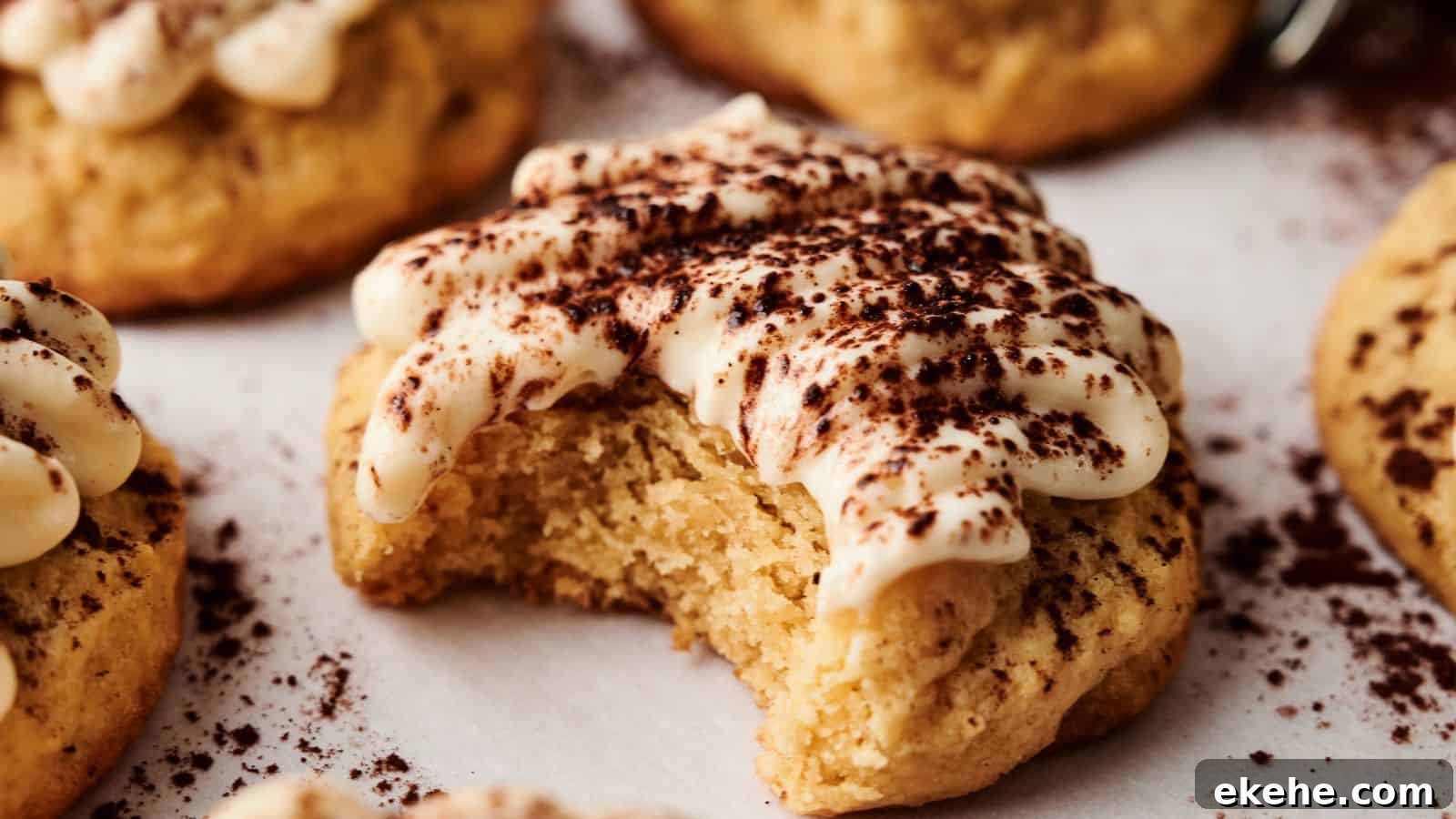 A soft cookie topped with cream and cocoa powder has a bite taken out of it. Other similar cookies are visible in the background.