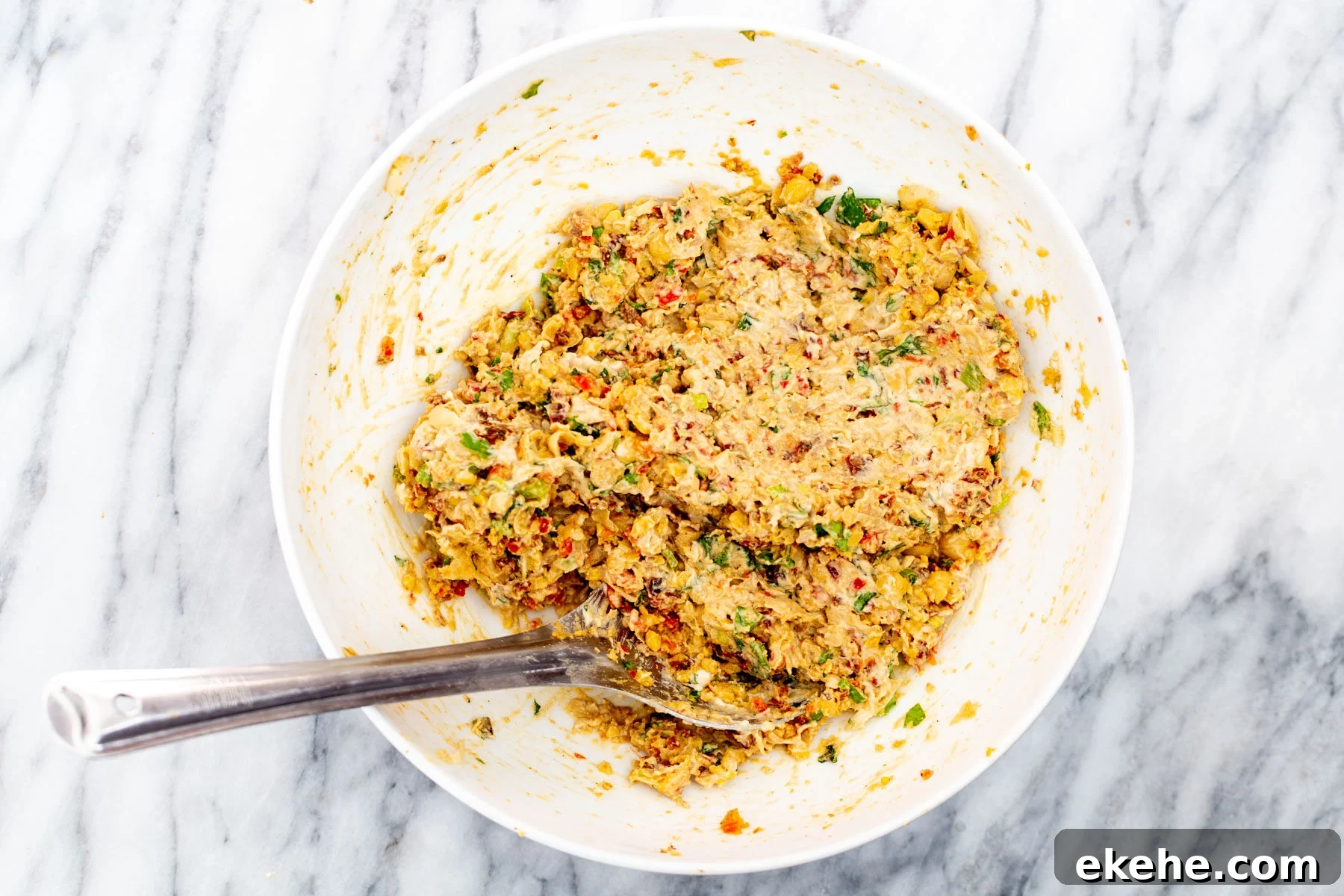 smashed chickpeas being mixed with veggies and lemon tahini dressing 