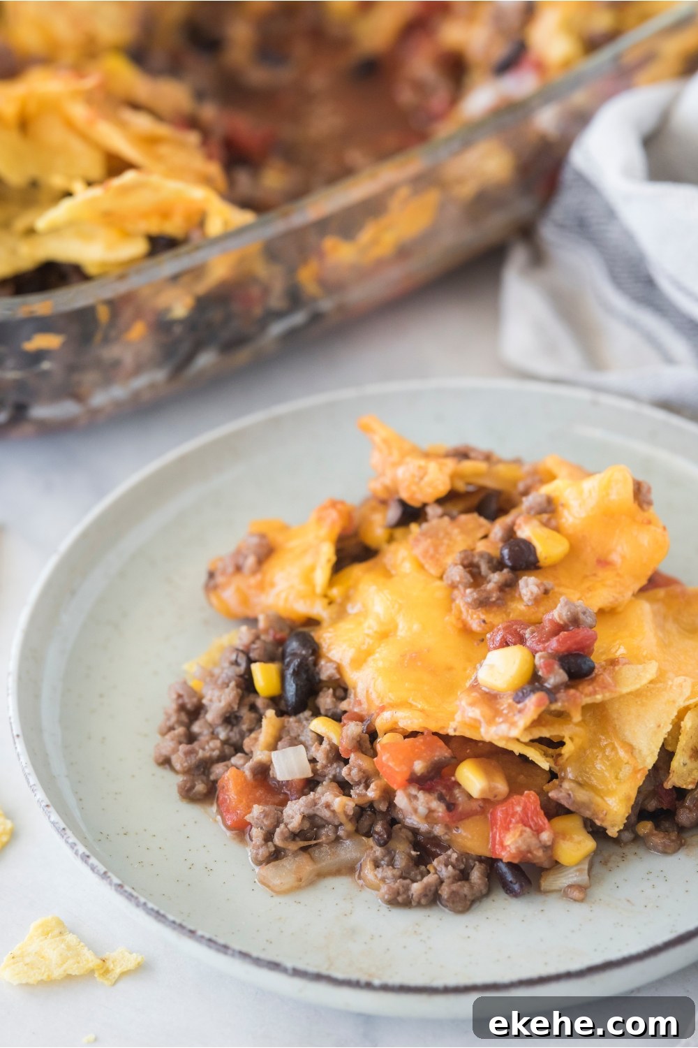 A serving of Tex-Mex casserole piled high on a plate with the rest of the casserole in the background.