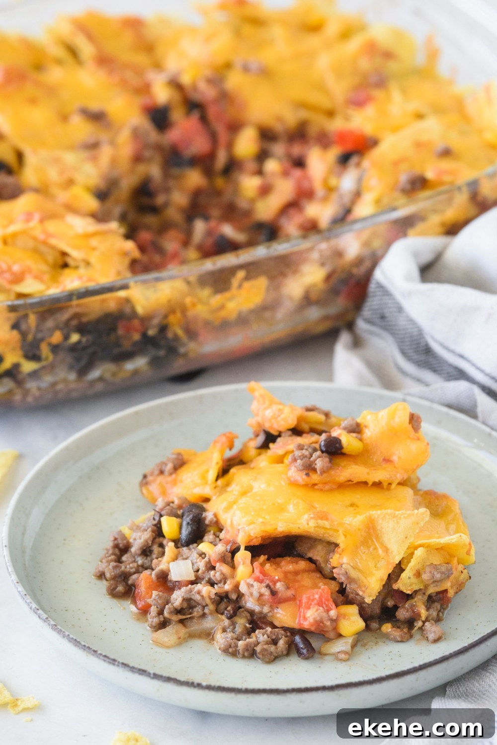A serving of Tex-Mex casserole piled high on a plate with the rest of the casserole in the background.