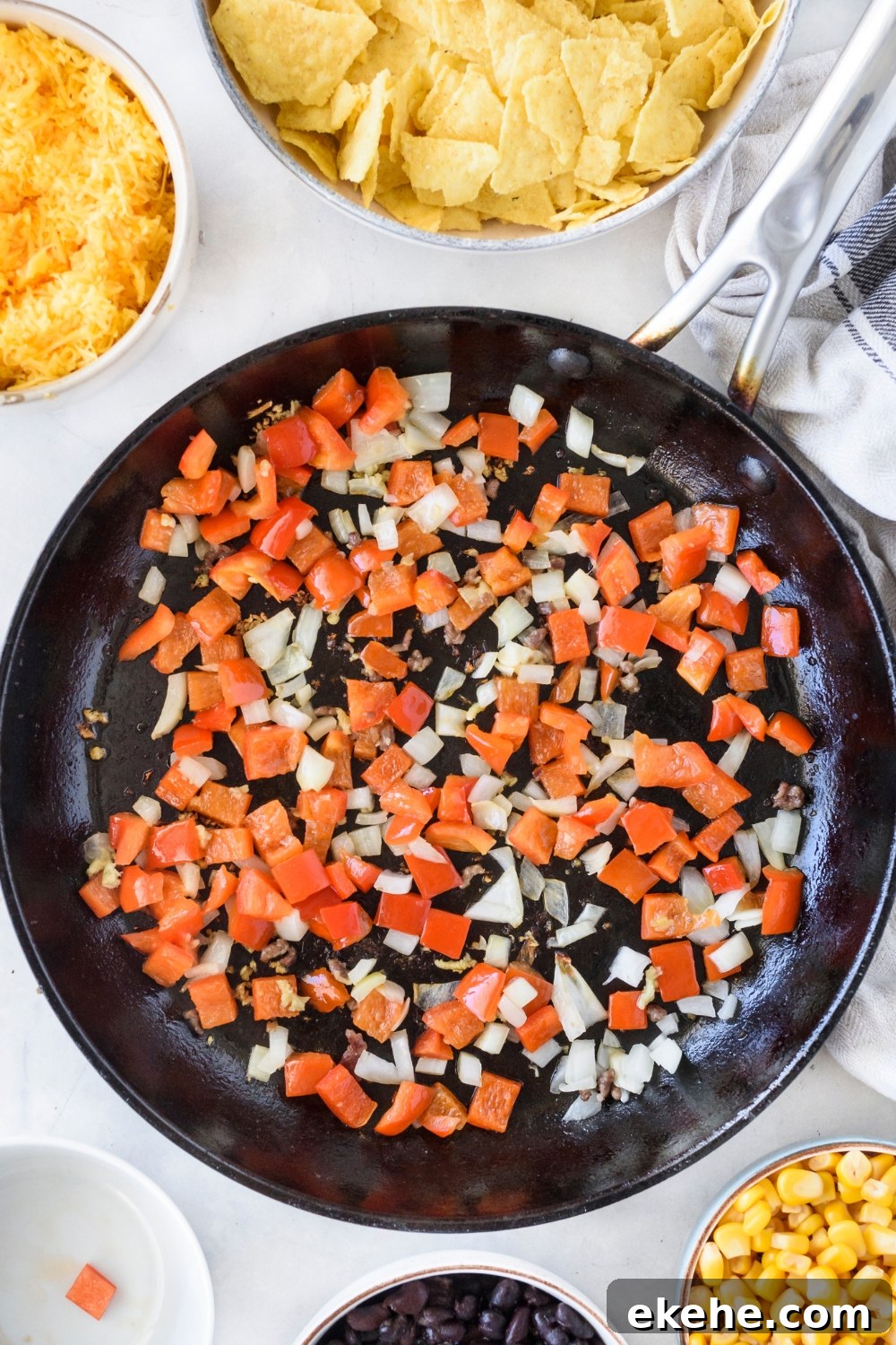 A skillet filled with diced red peppers and diced onion cooking in oil.