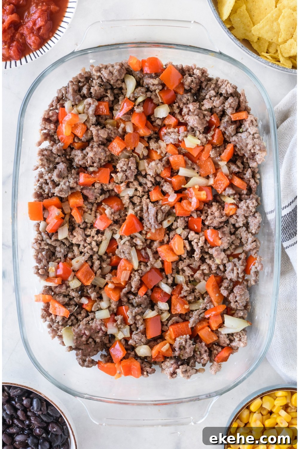 A clear baking dish filled with cooked ground beef, diced red peppers, and diced onion.
