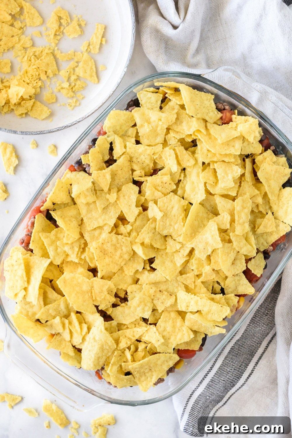 A clear baking dish filled with unbaked casserole covered in crushed tortilla chips.