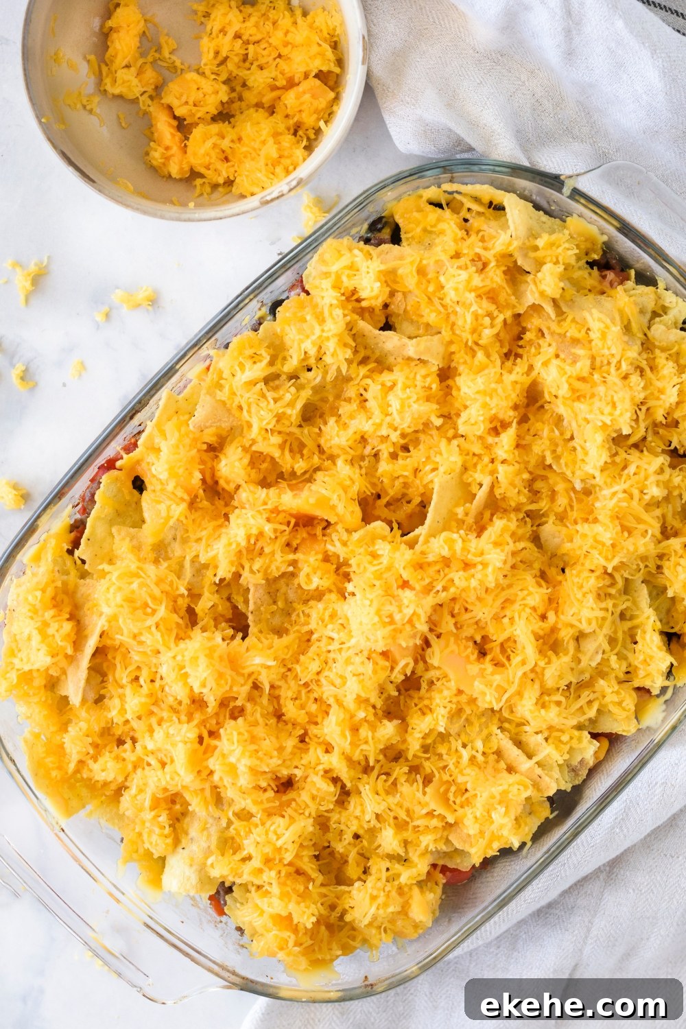 A clear baking dish filled with unbaked casserole covered in shredded cheese.