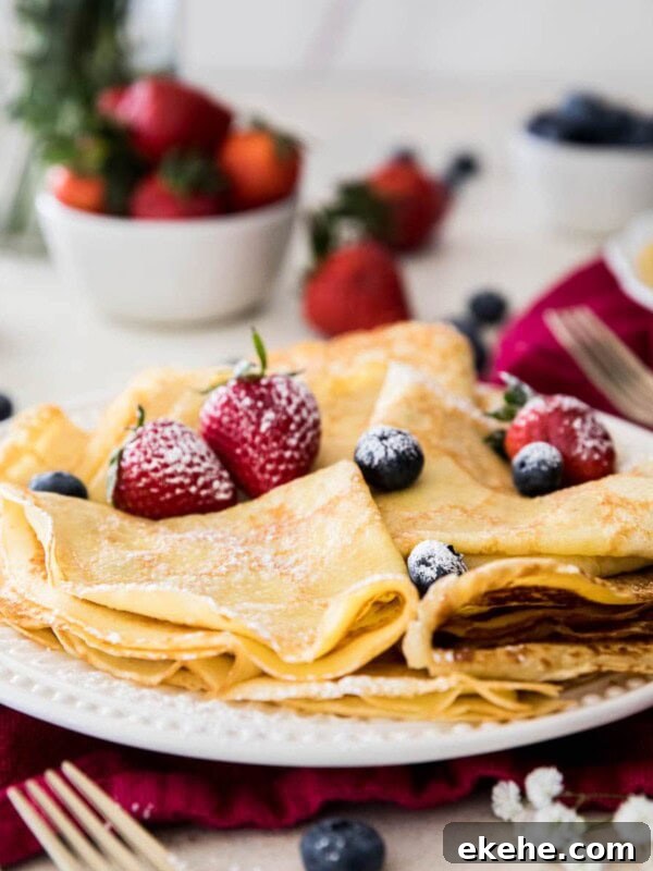Fluffy Sourdough Pancakes Recipe for Crispy-Edge Breakfast 10 folded crepes with powdered sugar and strawberries on a white plate