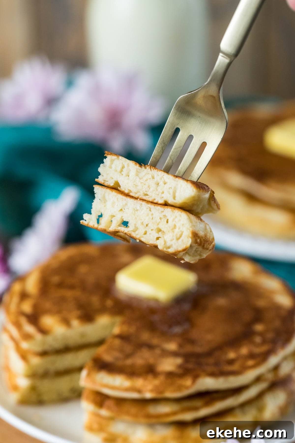 Fluffy Sourdough Pancakes Recipe for Crispy-Edge Breakfast 6 Fork with a bite of pancakes taken from a tall stack of buttered pancakes in the background.