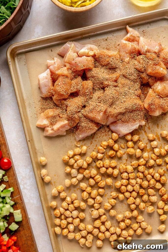 Raw chicken breast and chickpeas seasoned with Greek spices on a sheet pan before roasting