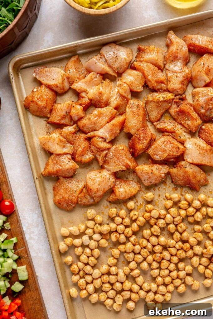 Greek chicken and chickpeas roasting on a parchment-lined sheet pan in the oven