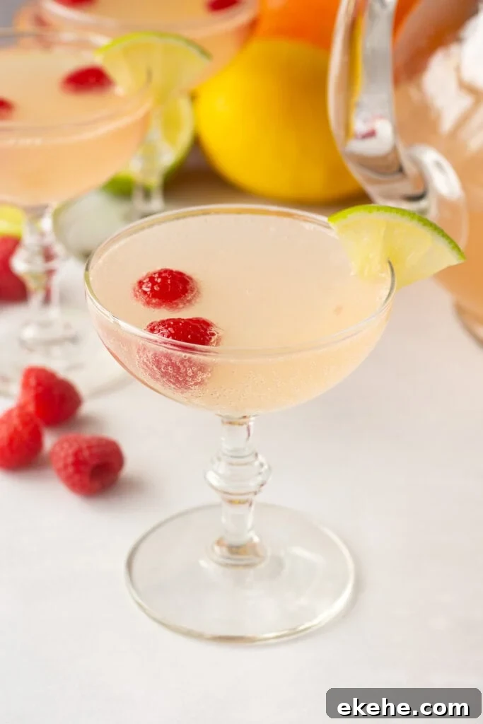 a pink mocktail in a champagne glass with citrus fruit and raspberries in and around it.