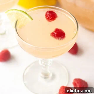 an angled shot of a pink mocktail in a low champagne glass with raspberries and a lime wedge in it.