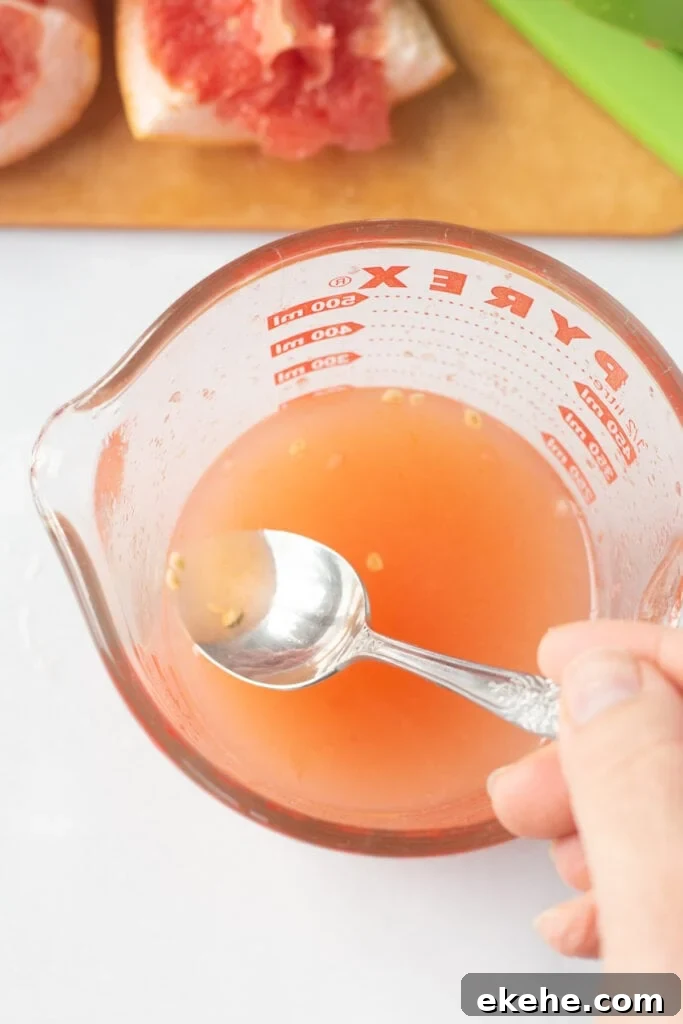 a spoon removing seeds from freshly squeezed grapefruit juice in a measuring cup.