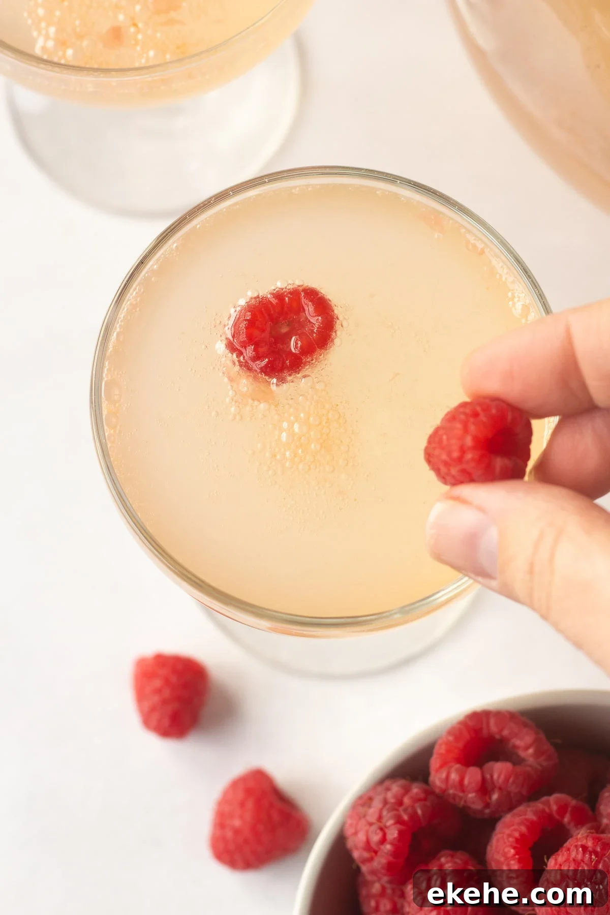 placing fresh raspberries into a champagne glass with pink liquid in it.