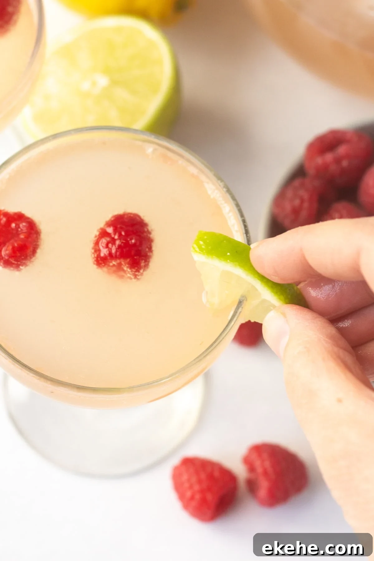 a hand placing a lime wedge on the rim of a champagne glass with a pink drink in it.