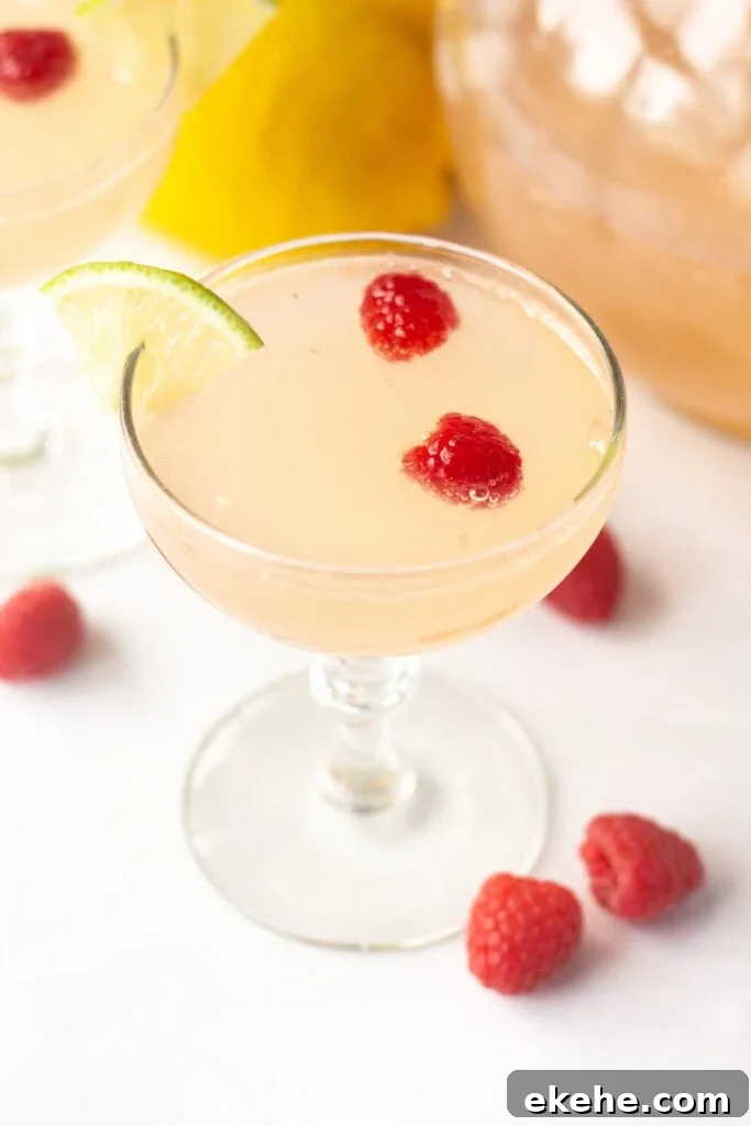 an angled shot of a pink mocktail in a low champagne glass with raspberries and a lime wedge in it.